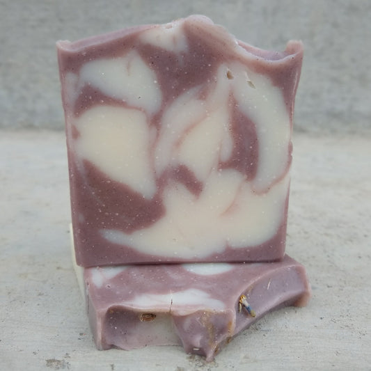 A bar of Clean Lavender soap sits on top of a second bar laid over. The soap is a swirl of purple and white against a light gray background